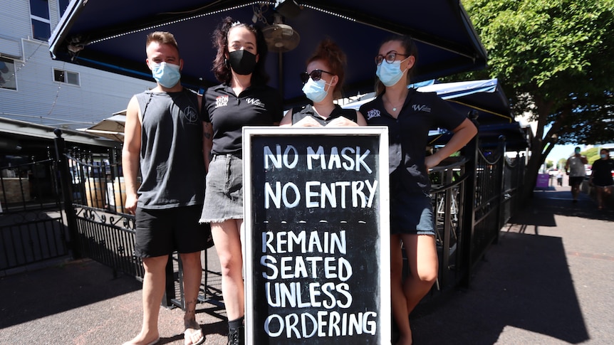 People stand out the front of a pub which says 'No mask, no entry'
