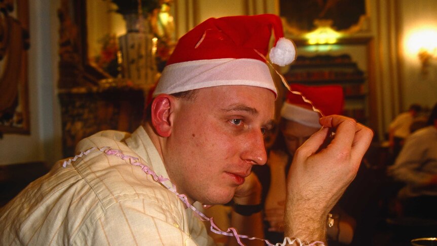 A close shot of a man looking melancholy and wearing a santa hat.
