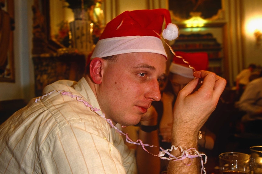 A close shot of a man looking melancholy and wearing a santa hat.