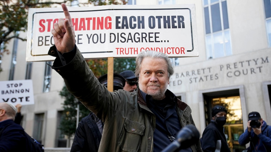 A man pointing with his arm raised in front of a sign which reads "stop hating each other because you disagree..."