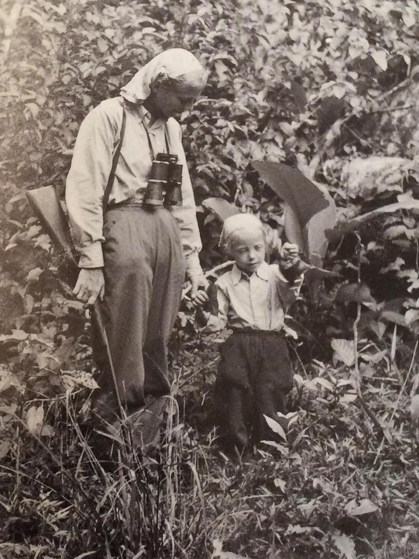 A black and white image of a woman holding hands with a little blonde girl in the jungle