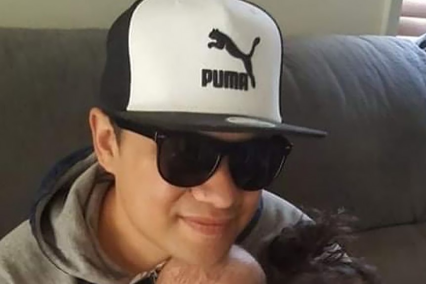 A man in sunglasses and a Puma hat smiles. 