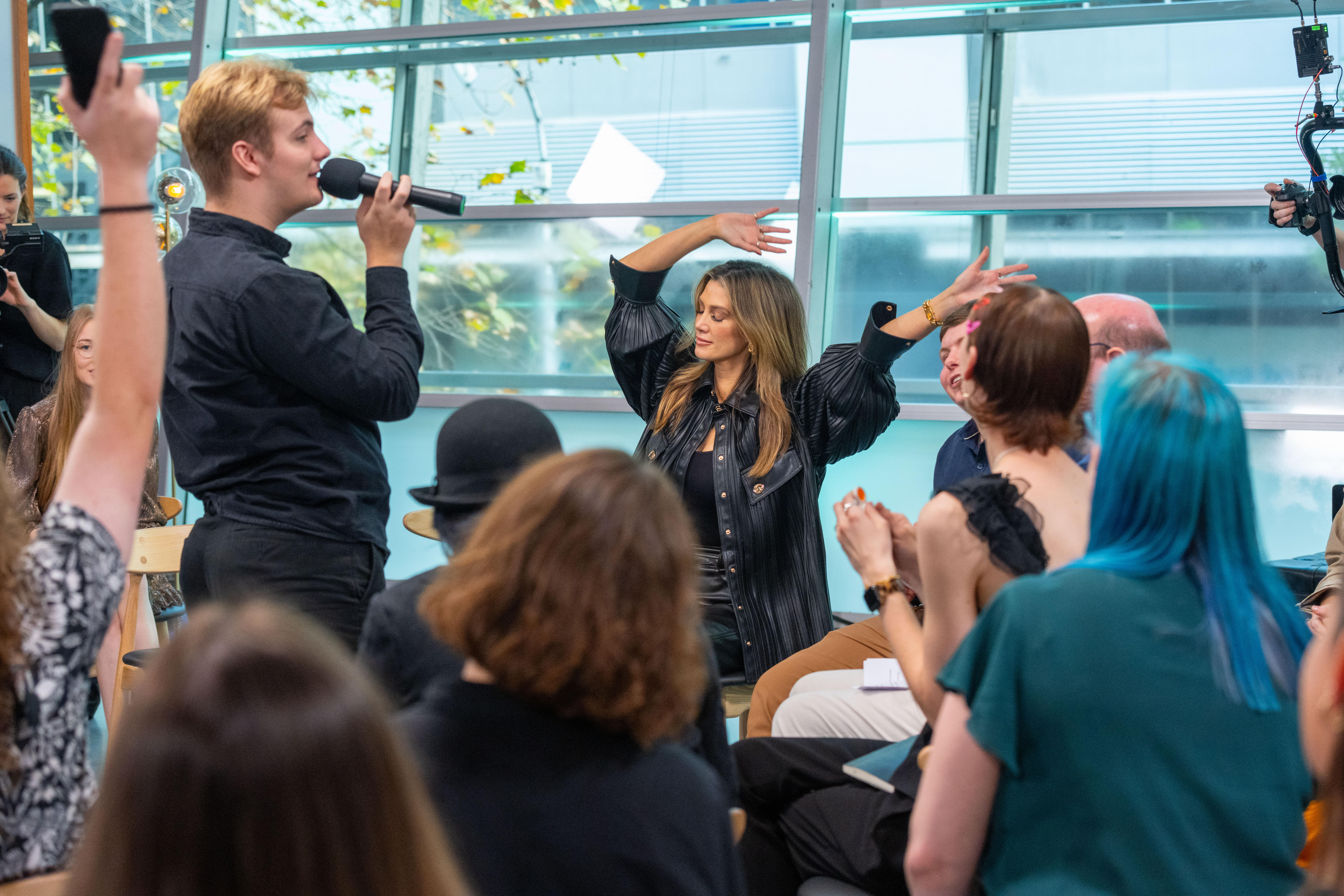 Delta Goodrem sits with eyes closed and arms in the air while a teenage boy with blond hair sings into microphone.