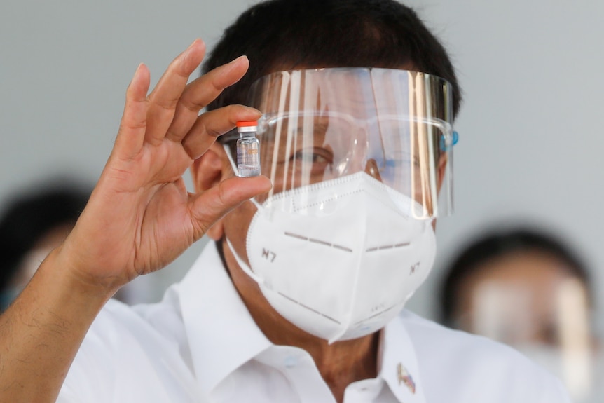 President Duterte of the Philippines wears a mask and face-shield while holding up a vial of vaccine.