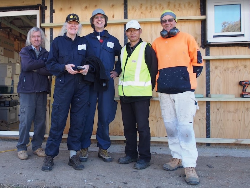 Five members of the community wearing tradesman's clothes outside a shed