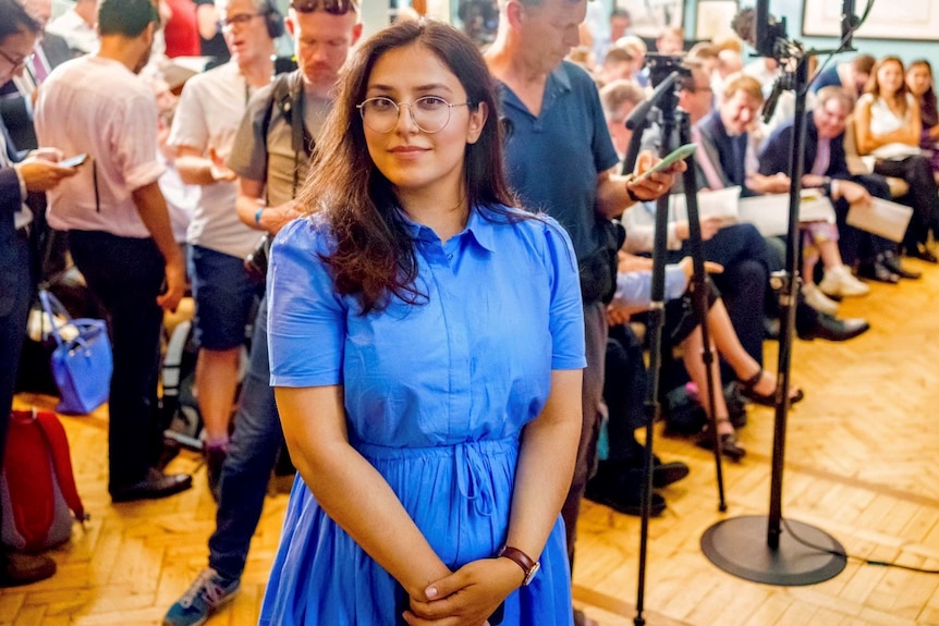 Shabnam wearing a blue dress standing in front of a crowd of reporters.