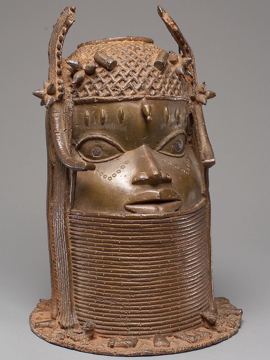 A brass statue of the head of a King, around their neck are beaded rings.