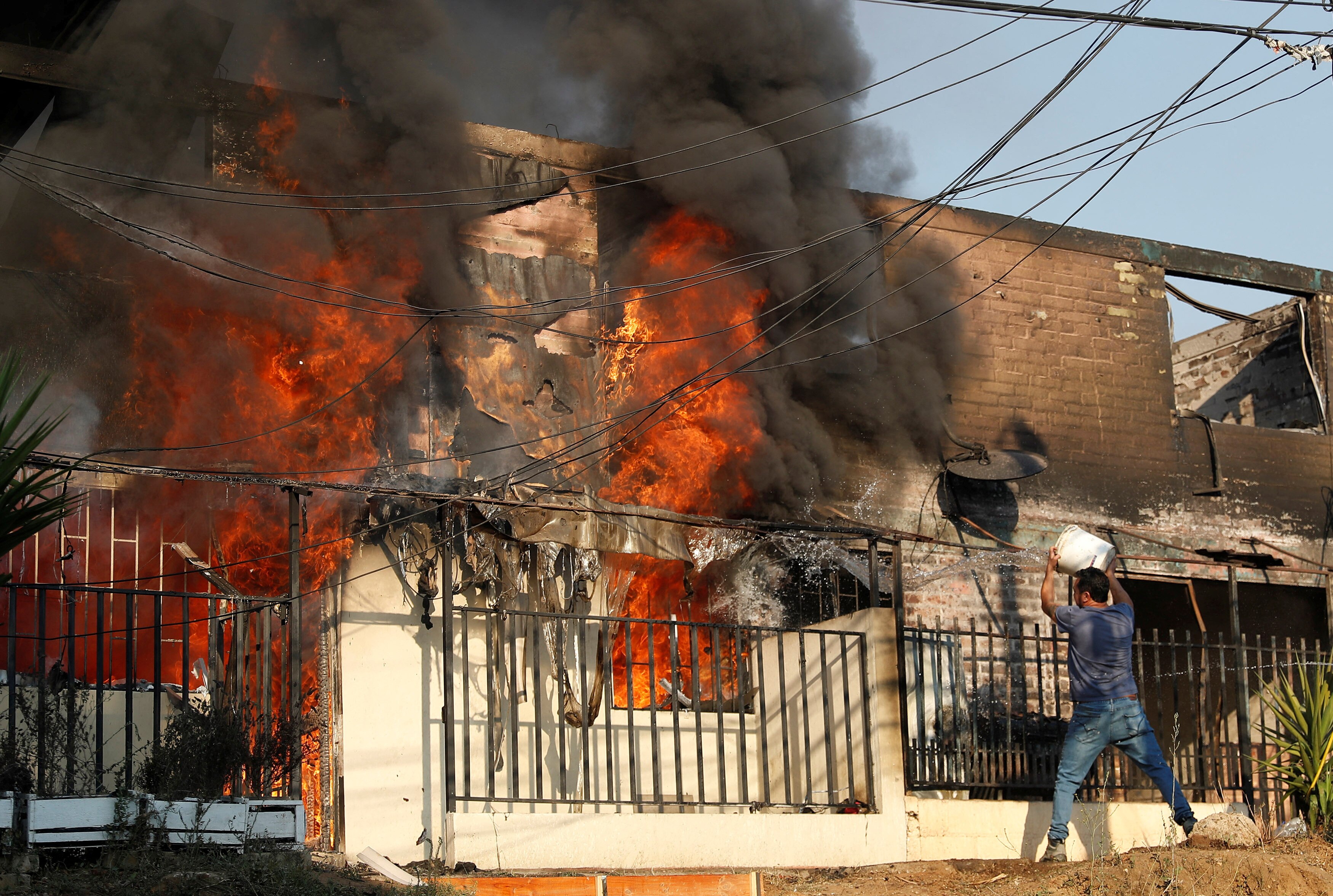 A man pours a bucket of water on a burning building.