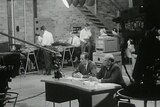 Black and white shot of Charlton sitting at desk in studio with ABC TV cameras around him and production staff in background.