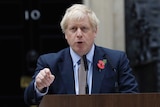 Boris Johnson stands at a podium pointing outside 10 Downing Street.