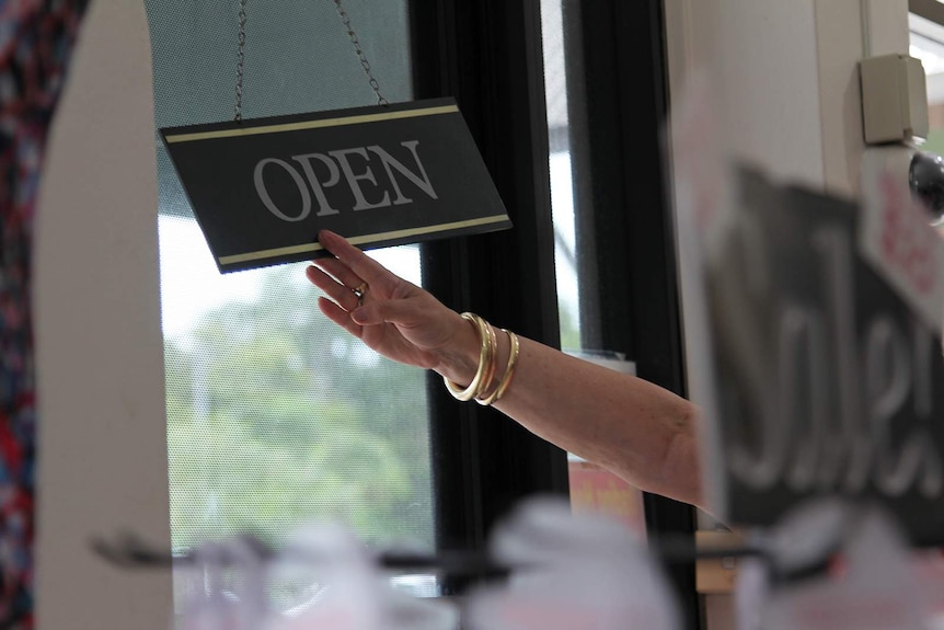 A hand turning an open sign so it faces the closed sign.