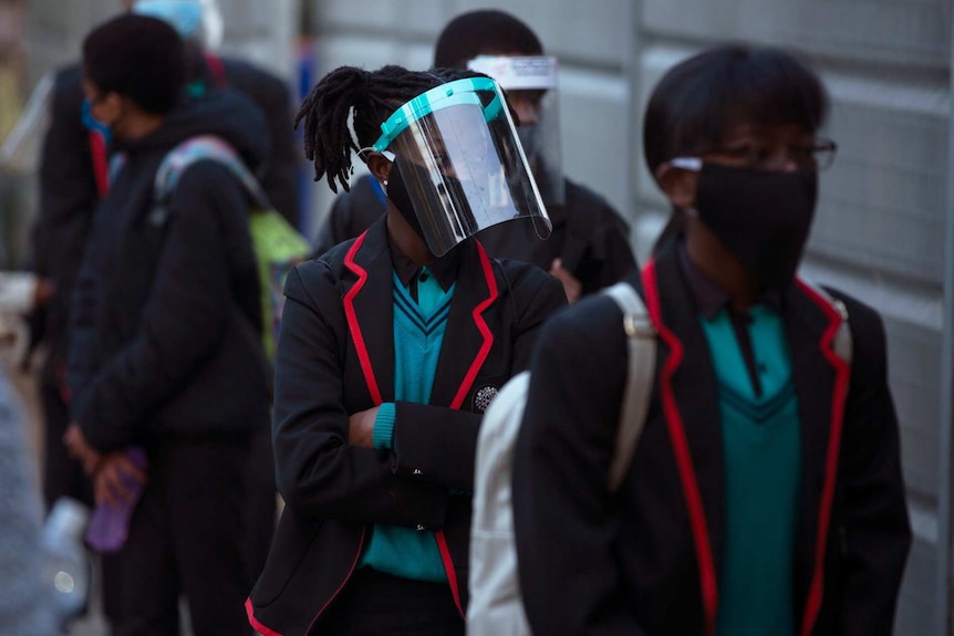 children in school uniforms, masks and face shields wait in line