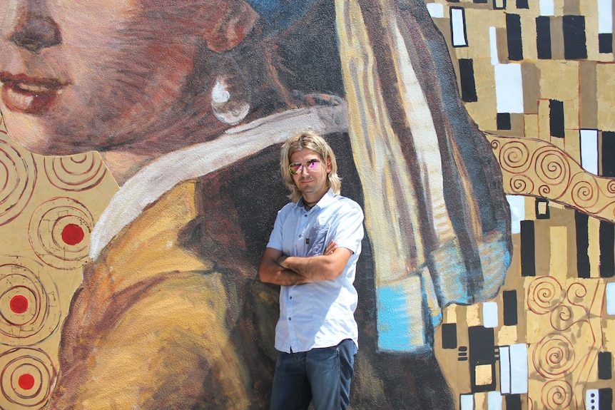 A man stands in front of an outdoor mural