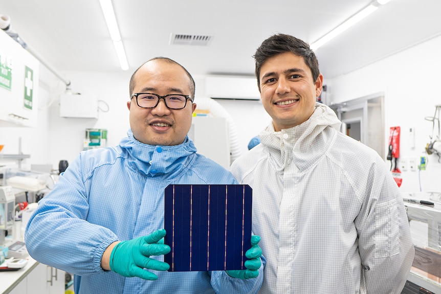 David Hu and Vince Allen wear protective suits and hold a solar cell.
