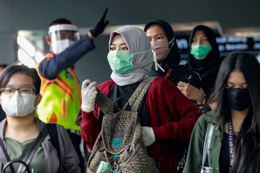 Indonesian women wearing head cover and mask in the crowd.