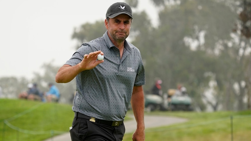 A cap-wearing golfer waves at the crowd while holding his ball after making a birdie at the US Open.