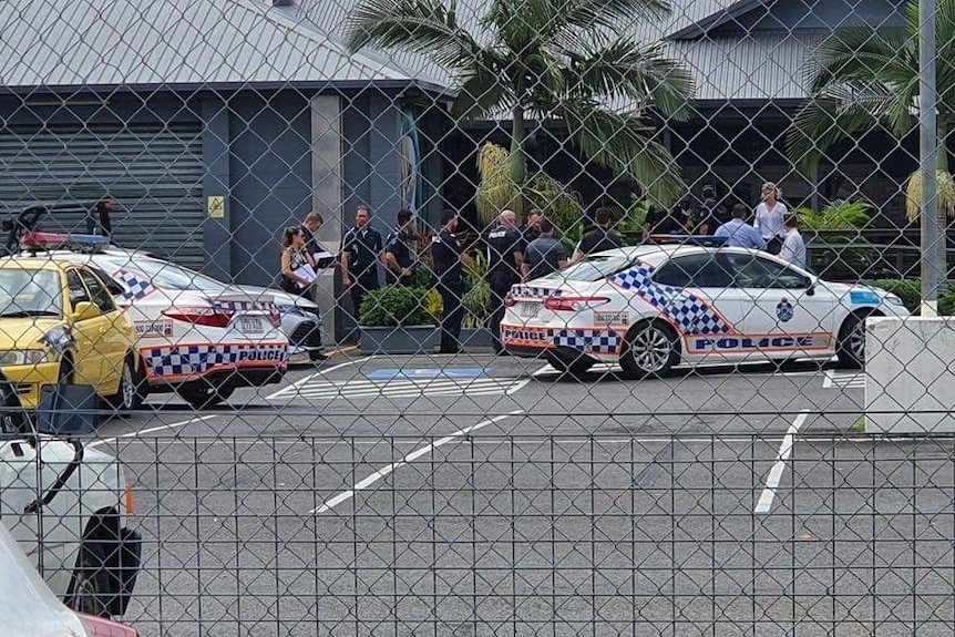 Police officers and cars seen through a chicken wire fence.