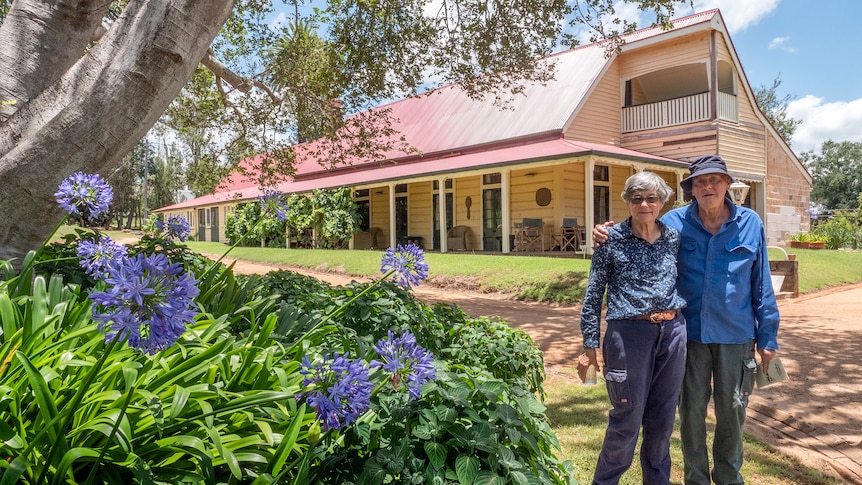 A man and woman stand outside a Queensland style homestead.