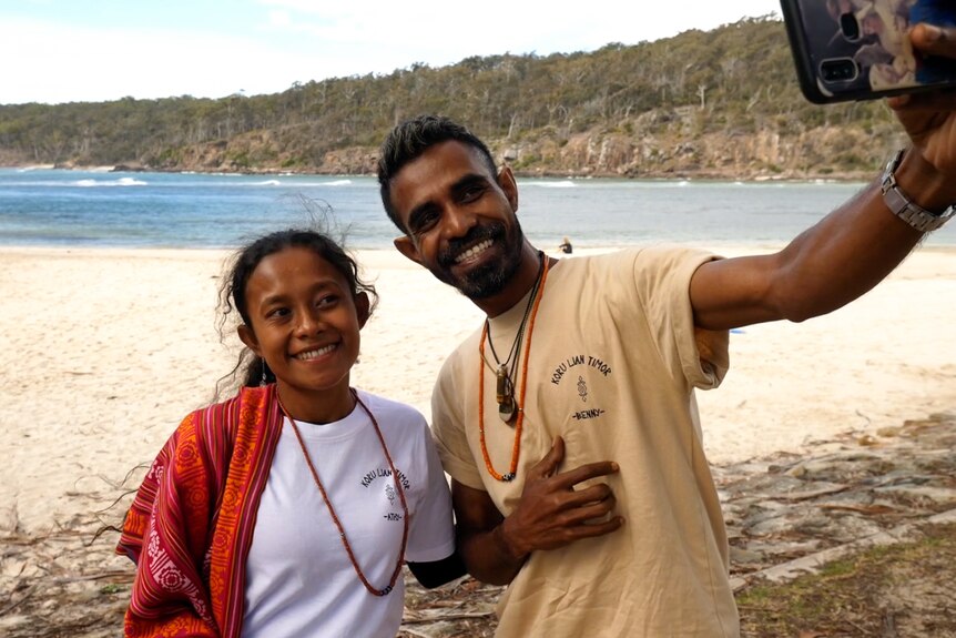 Young East Timorese girl and man taking a selfie with beach and bush in background.