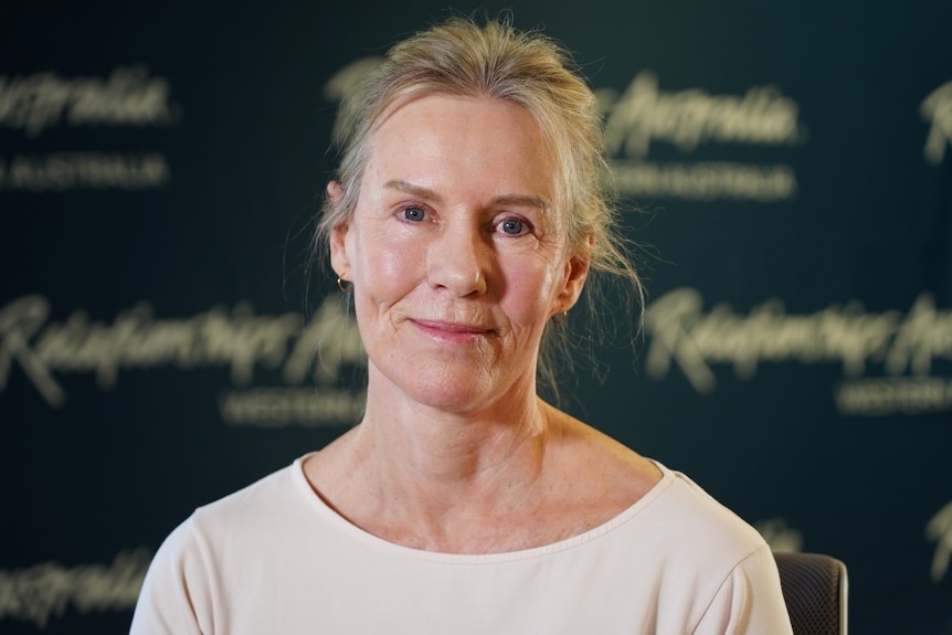 A blonde middle aged woman stands in front of an agency branding backdrop 