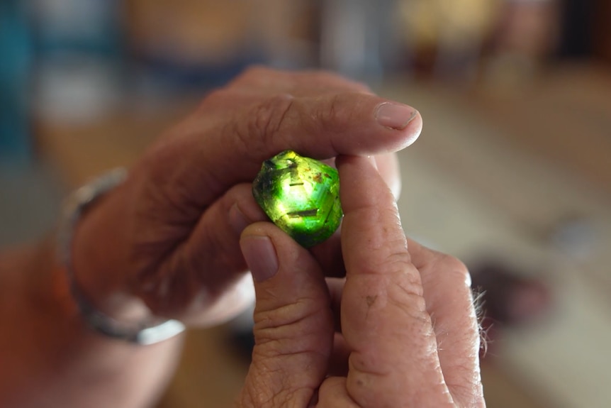 Close up of man holding uncut green gem the size of aa 50-cent piece