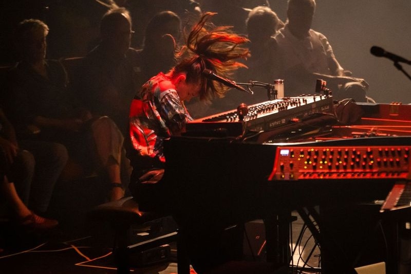 A performer onstage thrashes their hair while at the keyboards.
