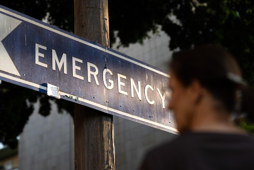 A blurry image of a woman standing in front of an emergency hospital sign
