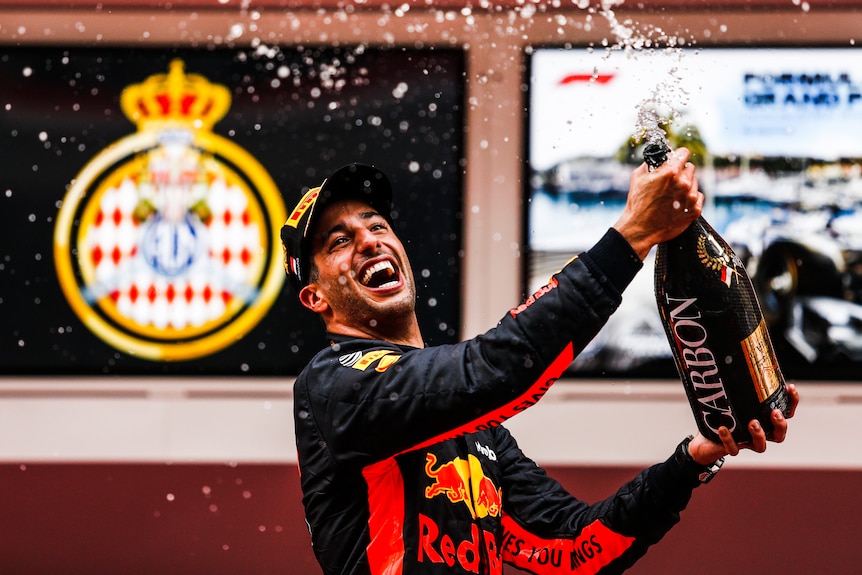 F1 driver Daniel Ricciardo celebrates by spraying champagne while standing on a podium, after winning a race.