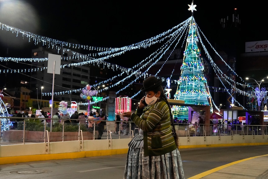 a woman is talking on her cell phone in front of a christmas tree and christmas lights are displayed in La Paz