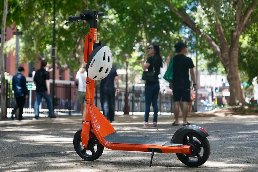 La scooter eléctrica naranja se dejó estacionada en un camino con peatones caminando al fondo en South Brisbane.