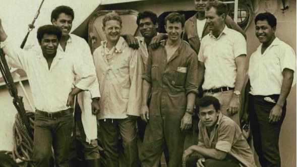 A black and white shot of nine men standing on a boat.