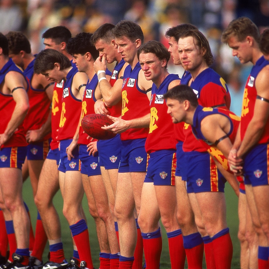 A group of AFL players look down at the ground as they observe a minute's silence before a game.