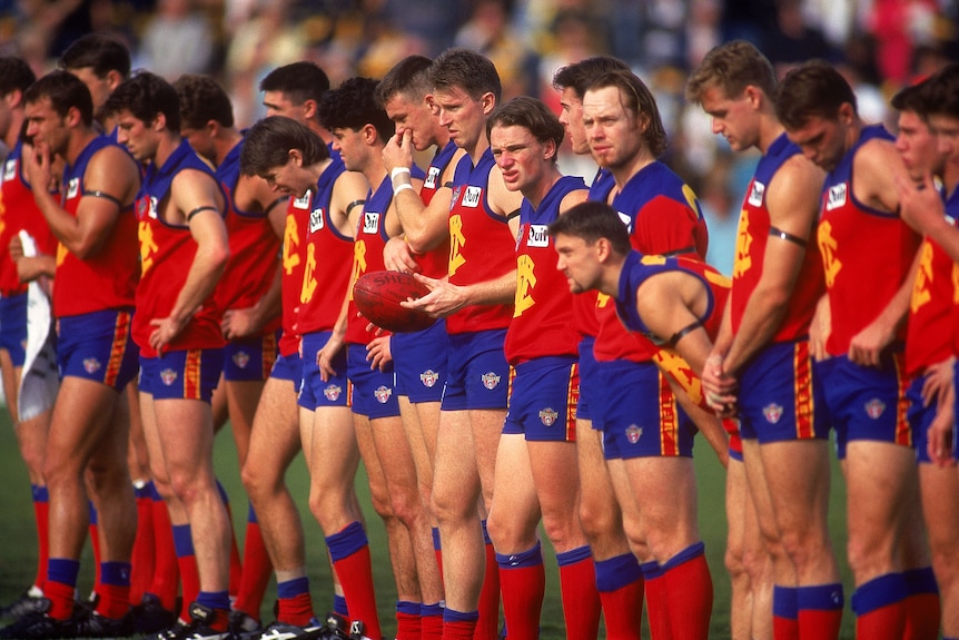 A group of AFL players look down at the ground as they observe a minute's silence before a game.