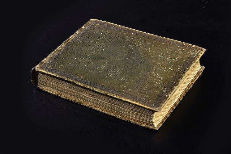 A close-up shot of an old brown hardcover journal on a black background.