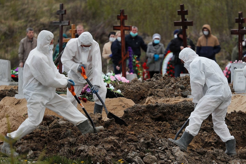Men in PPE digging a grave while people in face masks watch on