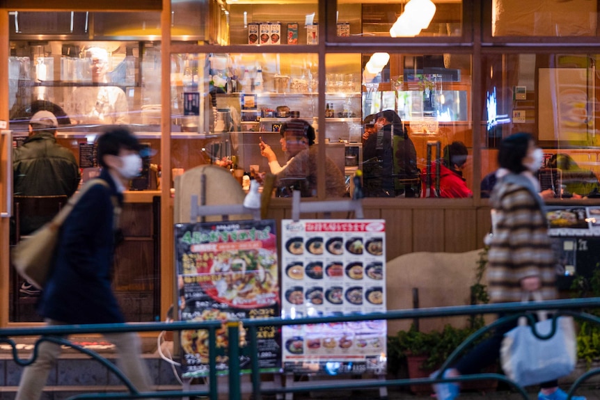 A crowded restaurant in Tokyo with people outside in face masks