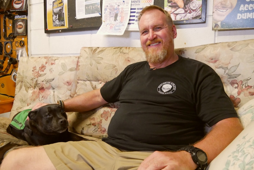 Man sits on couch with dog and smiles at camera
