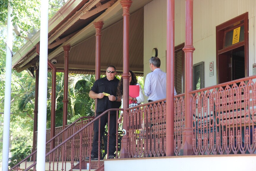 Man on steps looking at camera dressed in black standing next to his lawyer.