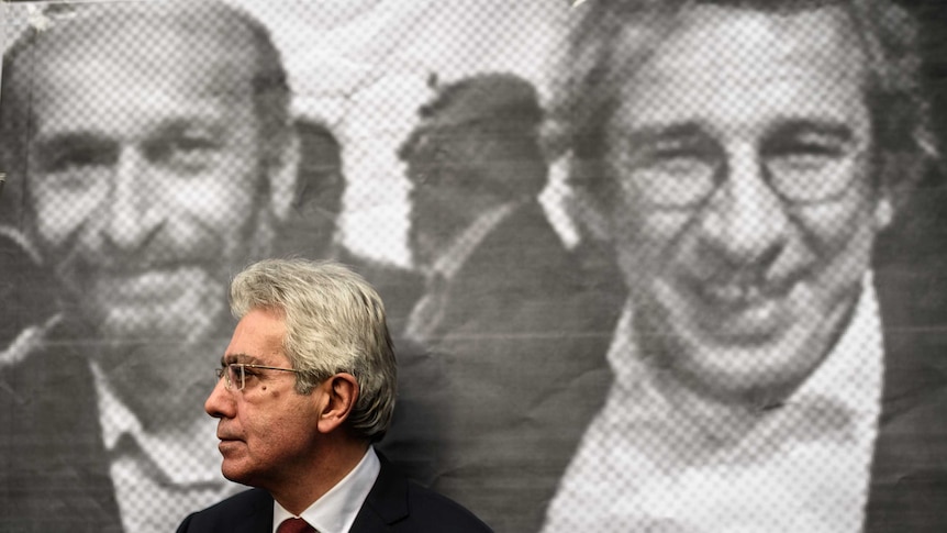 A man stands in front of a poster of Can Dundar and Erdem Gul.