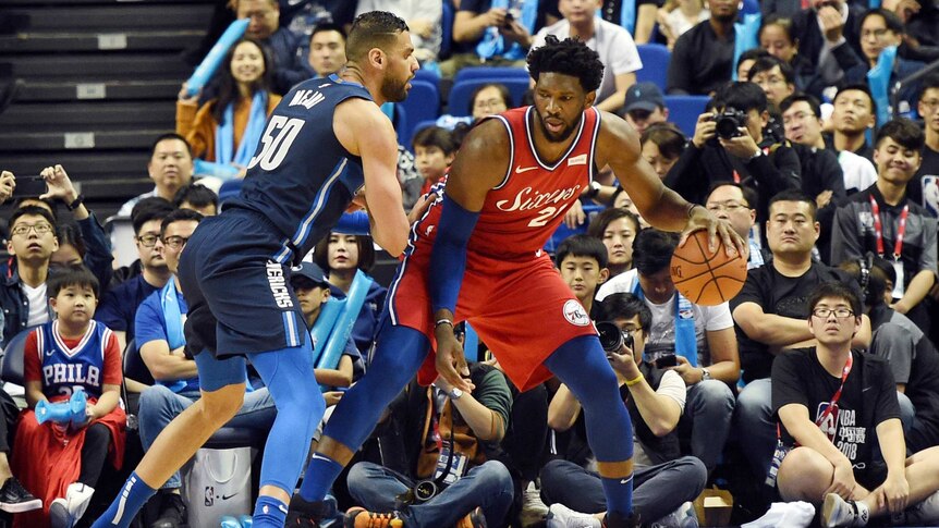 Two NBA players compete for the ball as a crowd looks on at courtside in Shanghai.