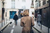 Photo of the back of a woman with short hair walking down a narrow street, with other people.