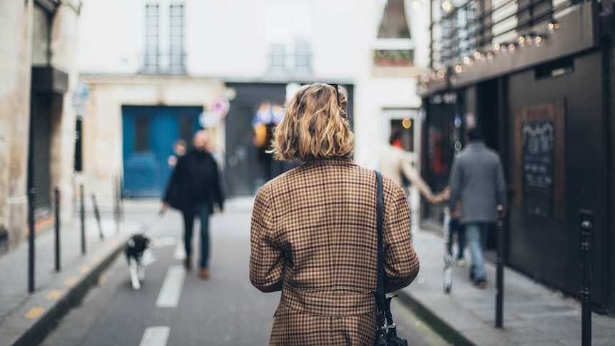 Photo of the back of a woman with short hair walking down a narrow street, with other people.