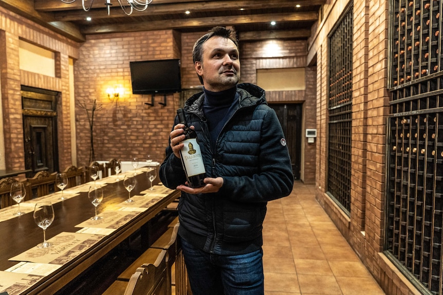 A man in a wine cellar holds up a bottle of wine.