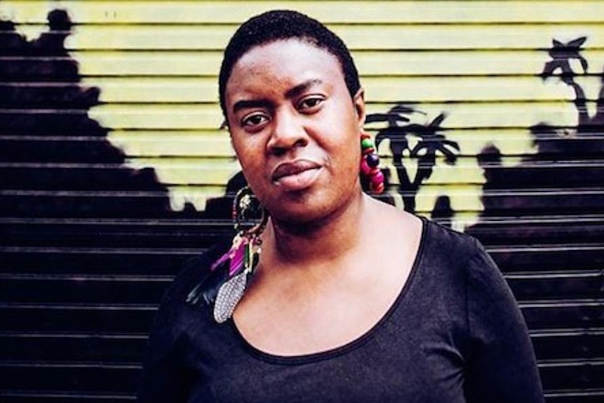 Maxine Beneba Clarke stands in front of a wall.