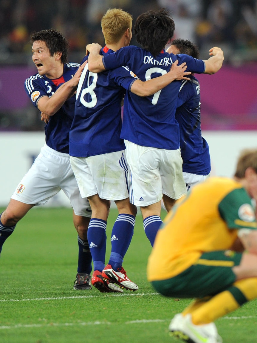 Shattered: Socceroos defender David Carney cuts a lonely figure as Japan's kings of Asia celebrate.