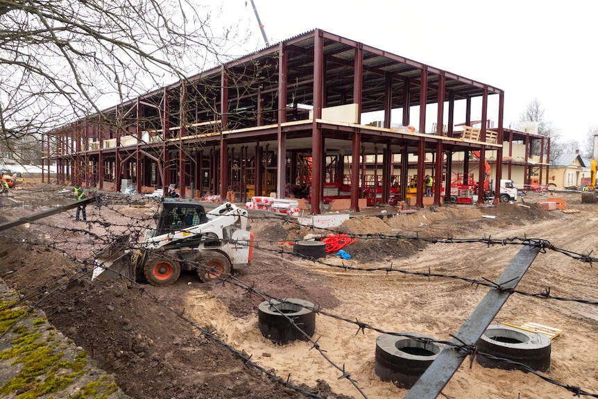 A large structure being built behind a thick barbed wire fence