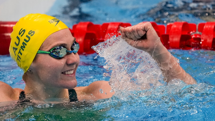 Ariarne Titmus at the end of the pool smiles while holding one fist in the air in celebration.