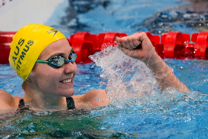 Ariarne Titmus at the end of the pool smiles while holding one fist in the air in celebration.