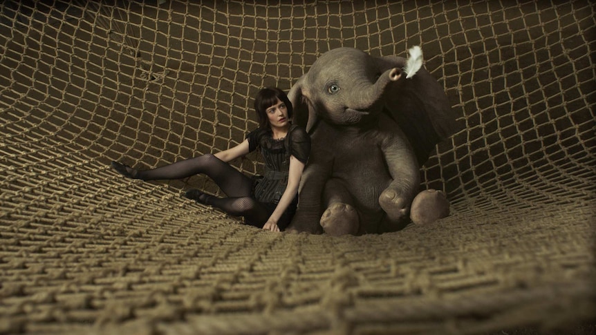 The actor and the CGI animated elephant sit side by side in a crash net looking at a floating white feather.