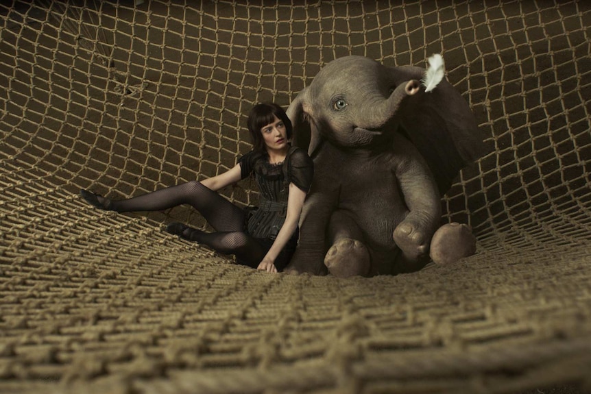 The actor and the CGI animated elephant sit side by side in a crash net looking at a floating white feather.